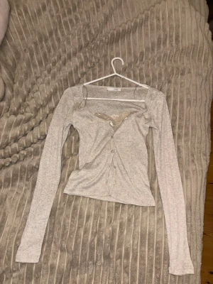 Beige långärmad kofta med spetsdetalj - Snygg beige kofta med lång ärm och djup urringning. Framtill finns en dekorativ spetsdetalj vid bysten och knäppning med små knappar. Modellen är figurnära och passar perfekt till jeans eller kjol. absolut skitsnygg ❤️❤️