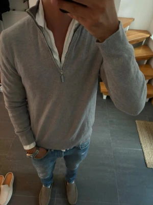 Ljusgrå halvzip tröja från Gran Sasso - Snygg ljusgrå tröja med halvzip och hög krage. Tillverkad i mjuk ullmix som känns skön mot huden. Tröjan har ribbade muddar vid ärmslut och nederkant, perfekt att bära över en skjorta för en clean look. Lite för lite för modellen på bilden som är 180 cm och 65 kg