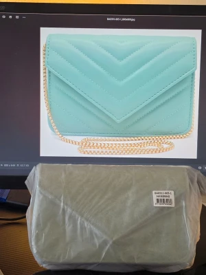 Mintgrön quiltad handväska med kedja - Snygg mintgrön handväska med quiltat mönster och guldfärgad kedjerem. Väskan har ett kuvertformat lock och stilren design som ger en modern touch till din outfit. Tillverkad i konstläder för en trendig look.