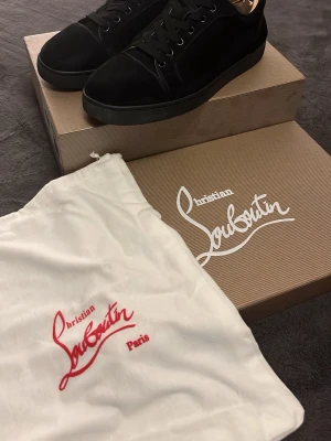 Svarta sneakers från Christian Louboutin - Snygga svarta sneakers från Christian Louboutin med klassisk röd sula och stilren design. Skorna har snörning och är tillverkade i skinn och mocka för en exklusiv känsla. Perfekta för dig som vill ha något extra till din outfit.