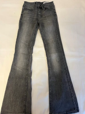 Grå bootcut jeans med utsvängda ben - Snygga grå bootcut jeans med utsvängda ben och klassisk femficksmodell. Jeansen har en tvättad look med subtila slitningar och är tillverkade i ett mjukt denimtyg. Perfekta för dig som gillar retrovibbar och vill ha ett par jeans som sticker ut. Storlek S, längd 32 