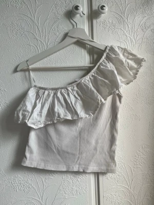 Vit offsoulder med volang från ZARA - Snygg vit omffsoulder från ZARA med bred volang. Toppen är lätt ribbad och har en offshoulder-design som ger en trendig look. Perfekt för varma dagar och somriga outfits.