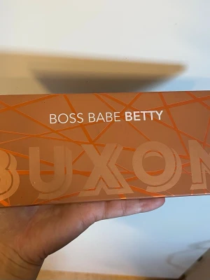 Buxom Boss Babe Betty ögonskuggspalett - Snygg ögonskuggspalett från Buxom med namnet Boss Babe Betty. Paletten innehåller 12 olika nyanser, perfekta för att skapa både neutrala och glamorösa looks. Färgerna går i varma toner och paletten har en stilren, orange design med grafiskt mönster. Några av färgerna är endast testade! 