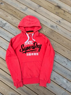 Superdry hooodie ~ Vintage  - Säljer denna Superdry hoodie i mycket bra skick och som är Vintage så är eftertraktad. Passar perfekt för dig som är mellan 178-187! Hör av er vid frågor eller minsta fundering 🙌  Längd: 70,5 cm  Bred: 57,5 cm  Ärm: 68 cm