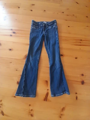 Blå bootcut jeans med fickdetaljer - Snygga blå bootcut jeans med klassiska fem fickor och dekorativa sömmar på bakfickorna. Jeansen har låg midja och utsvängda ben, perfekta för en retroinspirerad look. Tillverkade i denim med lätt stretch för skön passform.