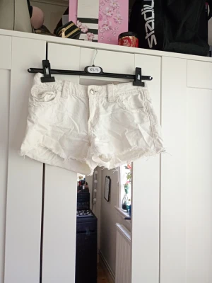 Vita jeansshorts med fransig kant - Säljer ett par vita jeansshorts i storlek XS. Det är passform 158 cm.Shortsen har rå, fransig kant nertill, klassisk femficksmodell och bälteshällor. Perfekta för sommaren och ger en avslappnad vibe till din outfit.💕