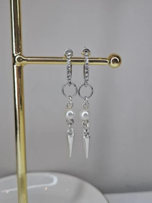 Silvriga örhängen med pärlor och spikes - Snygga silvriga örhängen med små gnistrande stenar på ringen, vita pärlor och spetsiga spikes som hänger ned. Perfekt accessoar för dig som gillar en mix av klassiskt och edgy stil. Ej rostfria