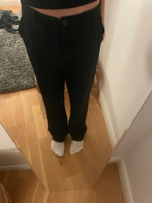 Svarta raka kostymbyxor - Säljer ett par svarta kostymbyxor med rak passform och hög midja. Byxorna har knapp och dragkedja framtill samt sidfickor. Perfekta för en clean och stilren look. Materialet är mjukt lite stretchig blandning.