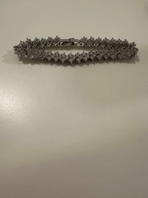 Silverfärgat armband med gnistrande stenar - Snyggt armband i silverfärg med massor av små, gnistrande stenar som ger en lyxig känsla. Armbandet har ett klassiskt och elegant mönster med stenar satta tätt intill varandra. Perfekt för dig som gillar bling och vill sticka ut lite extra.