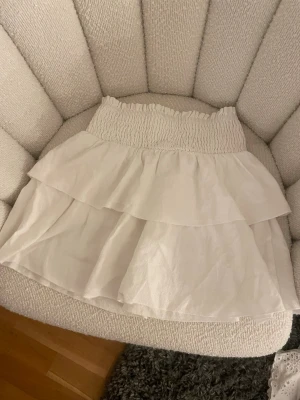Vit volangkjol från SHEIN - Supersöt vit kortkjol från SHEIN med bred smock i midjan och dubbla volanger. Kjolen är lätt och luftig, perfekt för varma dagar.