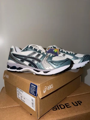 Asics Gel-Kayano 14 blå/vit sneakers - Snygga Asics Gel-Kayano 14 sneakers i blått, vitt och silver. Skorna har en sportig design med meshpaneler för bra ventilation och detaljer i metallic. Klassisk Asics-logga på sidan och vit sula med svarta detaljer. Perfekta för dig som gillar retrostil och streetwear. Storlek:44.                  Fraktas inom 24 timmar 