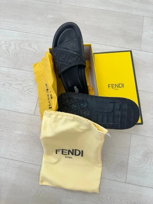 Svarta sandaler från Fendi - Snygga svarta sandaler från Fendi med klassisk logga på remmen. Tillverkade i slitstarkt material med bekväm sula och stilren design. Kommer med originalkartong och dustbag. Perfekta för en trendig och avslappnad look.