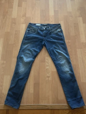 Mörkblå replay slim fit jeans - Snygga mörkblå slim fit jeans med slitningar och tvättade detaljer på låren och knäna. Klassisk femficksmodell med knappgylf och raka ben. Perfekta för dig som gillar en modern och avslappnad stil.W33,L32