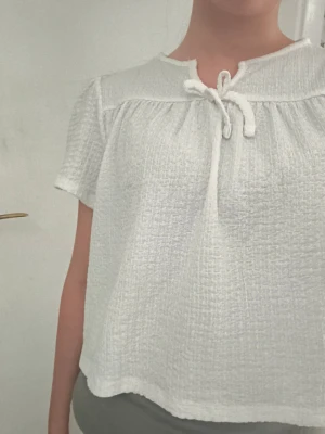 Vit kortärmad blus med rosett - Säljer en söt vit blus med korta ärmar och knyt i halsen pga att den passar inte mig längre. Toppen har en strukturerad, lite våfflad yta och en lös passform som ger en avslappnad vibe. Perfekt till jeans eller kjol för en enkel men stilren look. Jag har en likadan blus på plick fast i marinblå färg + en annan storlek om det skulle vara intressant! 