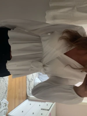Vit omlottblus med volang - Snygg vit omlottblus med volang nertill och knyt i midjan. Blusen har långa ärmar med resår vid ärmslut och en feminin v-ringning. Perfekt att styla med jeans eller kjol för en trendig look.