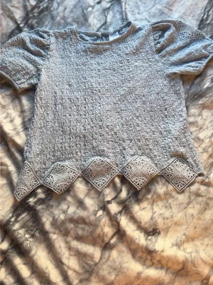Ljusblå blus med spetsdetaljer - Supersöt ljusblå blus med kort puffärm och spetskant nertill i ett zigzag-mönster. Blusen har en strukturerad yta och är perfekt för dig som gillar unika detaljer. Passar till både jeans och kjol för en trendig look.