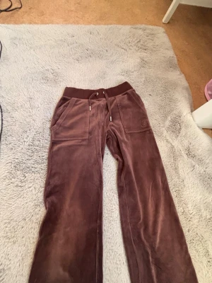 Bruna mjukisbyxor med dragsko - Säljer ett par bruna mjukisbyxor i mjukt velourmaterial. Byxorna har bred resårmidja med dragsko och stora fickor framtill. Perfekta för chill dagar och har en relaxed fit med raka ben.