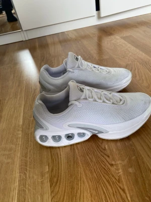 Vita Nike Air Max sneakers - Säljer ett par fräscha vita Nike Air Max sneakers med mesh-överdel och tydliga luftbubblor i sulan. Skorna har en sportig look med rund tå, vita snören och diskreta grå detaljer. Perfekta för dig som gillar stilrena och bekväma sneakers.