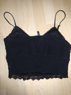 Svart spetsig croppad linnetopp - Svart spetslinne från Vero Moda i storlek M/T. Använt endast en gång, så det är i mycket fint skick. Justerbara axelband och mjukt, bekvämt material. Perfekt till fest och sommar.