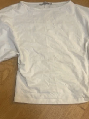Vit enkel topp med trekvartsärm - Klassisk vit topp med rund halsringning och trekvartsärm. Tillverkad i mjukt bomullstyg som känns skönt mot huden. Perfekt basplagg att styla med olika outfits. Enkel och stilren design utan synliga detaljer.