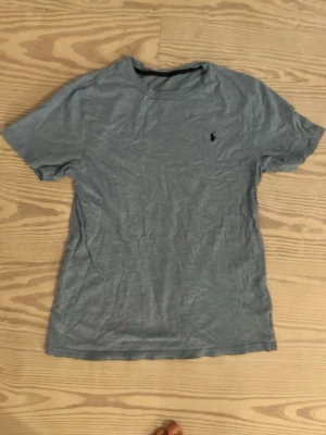 Grå basic t-shirt med logga - En enkel grå t-shirt i bomull med korta ärmar och en liten broderad logga på bröstet. Perfekt till jeans eller shorts för en avslappnad stil. Klassisk passform och rund hals.
