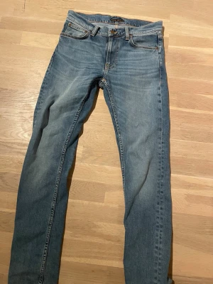 Blå raka jeans med broderade fickor - Säljer ett par klassiska blå jeans med rak passform och snygga broderade detaljer på bakfickorna. Jeansen har fem fickor, bälteshällor och stängs med knapp och dragkedja. Perfekta till vardags för en avslappnad look.
