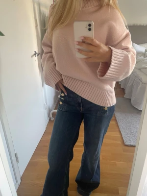 Ljusrosa stickad tröja - Mysig ljusrosa stickad tröja med breda ribbade muddar vid ärmslut och nederkant. Tröjan har en avslappnad, oversized passform och rund halsringning. Perfekt för att hålla sig varm och snygg under kyliga dagar.