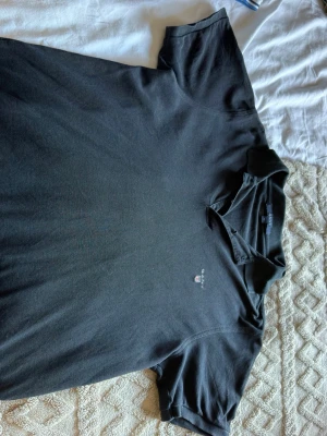 Svart pikétröja från Gant - Klassisk svart pikétröja från Gant med liten broderad logga på bröstet. Tröjan har krage och korta ärmar, perfekt till en avslappnad men ändå stilren look. Tillverkad i mjuk bomull för skön känsla hela dagen.