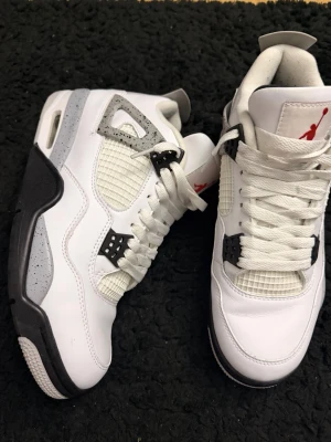 Vita och svarta Air Jordan sneakers - Säljer ett par sneakers i vitt med svarta och grå detaljer samt röd logga på plösen. Skorna har meshpaneler, robust sula och klassisk siluett. Materialet är en mix av läder och textil. Perfekta för dig som gillar streetwear och snygga detaljer.