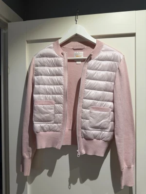 Ljusrosa quiltad cardiganjacka - Supersöt ljusrosa cardiganjacka med quiltade partier framtill och två fickor. Jackan har ribbade muddar, dragkedja och är tillverkad i en mjuk stickad kvalitet kombinerat med glansigt material på framsidan. Perfekt för lager på lager och en chill look.