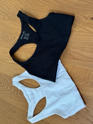 Svart och vit sport-bh från Move - Två sport-bhar från Move i svart och vitt. Båda har brottarrygg och är tillverkade i ett stretchigt material som passar perfekt för träning. Den vita har en liten logga framtill. Säljes som ett set.