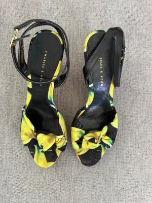 Charles & Keith kilklackade sandaler - Snygga kilklackade sandaler från Charles & Keith med svart och gul mönstrad textil framtill och svart ankelrem. Klacken är i kork med flätad detalj längst ner. Perfekta för dig som vill ha en färgklick och bekväm höjd på skon.