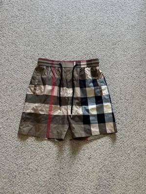 Burberry shorts - Ett par befor beige burberry bad shorts med rutig design. De är i storlek S och i helt nytt skick. Pris kan diskuteras och skriv om du har några frågor. 