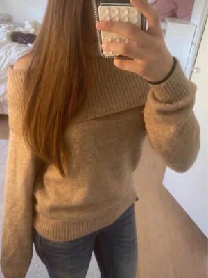 Beige off shoulder stickad tröja - Säljer en beige stickad tröja med bred ribbad off shoulder-krage. Tröjan har långa ärmar och ribbade muddar vid ärmslut och nederkant. Perfekt för dig som gillar en avslappnad men ändå trendig stil.