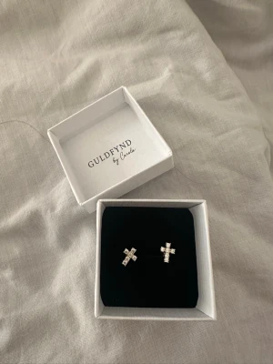 Örhängen evighet i äkta silver - guldfynd by Carola. OBS: helt oanvända! - Örhängen evighet i äkta silver - guldfynd by Carola. OBS: helt oanvända! Kommer med sin box   Örhängen EVIGHET i förgyllt äkta silver. Stiftörhängen formade som kors och fattade med Kubisk Zirkonia. Guld färgad.   Säljer även matchande armband.  Nypris: 500kr