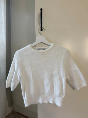 Vit stickad tröja från Zara - Säljer en vit stickad tröja från Zara med rund halsringning och halvlånga ärmar. Tröjan har en mjuk och fluffig struktur samt ribbade muddar vid ärmslut och nederkant. Det är ett tyvärr som en liten fläck precis vid halsen som inte syns jätte tydligt på kameran då jag försökt tvättat bort fläcken men den har inte riktigt försvunnit så säljs sen billigt då tröjan knappt är använd🌸.