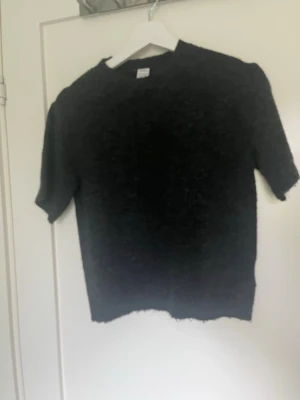 Mörkgrå stickad kortärmad topp - Mysig mörkgrå stickad topp med korta ärmar och rund hals. Perfekt för lager-på-lager och passar till både jeans och kjol. Enkel och stilren design som funkar till många olika looks.