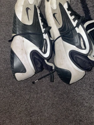 Nike Zoom 2K svartvita sneakers - Nike Zoom 2K sneakers i svart och vitt med futuristisk design och tydliga detaljer. Skorna har en chunky sula, mesh och syntetmaterial samt stora Swoosh-loggor på sidorna. Svarta snören och dragflik bak för enkel påtagning.