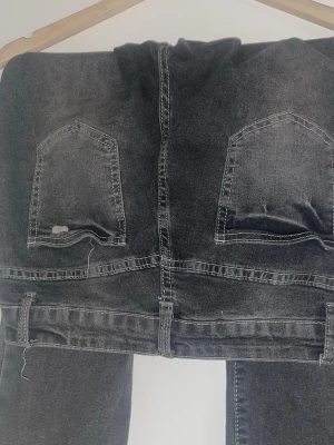 Mörkgrå raka jeans - Säljer ett par mörkgrå jeans med raka ben och klassiska bakfickor. Jeansen har tydliga sömmar och bälteshällor, perfekta för en avslappnad och stilren look. Materialet är slitstarkt och passar till många olika outfits. Lite slitna i hälarna 