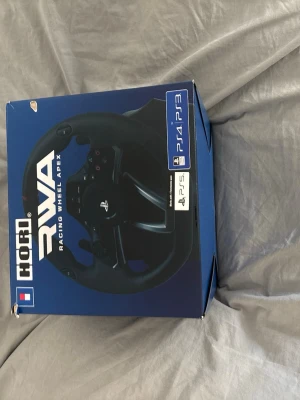 HORI RWA Racing Wheel Apex PS4/PS3/PS5/PC - Säljer en HORI RWA Racing Wheel Apex ratt och pedaler för PS4, PS3, PS5 och PC. Ratten är svart med klassisk racingdesign och flera knappar för spelkontroll. Perfekt för dig som vill ta bilspelen till nästa nivå med realistisk känsla.