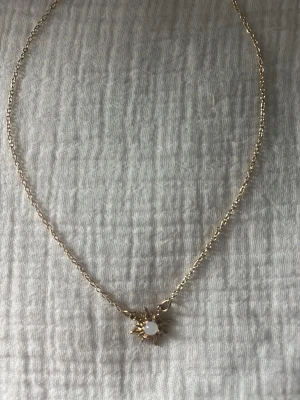 Guldhalsband med solhänge och pärla - Snyggt halsband i guldton med ett solformat hänge. I mitten av hänget sitter en rund vit pärla som ger en elegant touch. Kedjan är tunn och smidig, perfekt för att lyfta vilken outfit som helst. Passar dig som gillar unika detaljer och stilrena accessoarer.