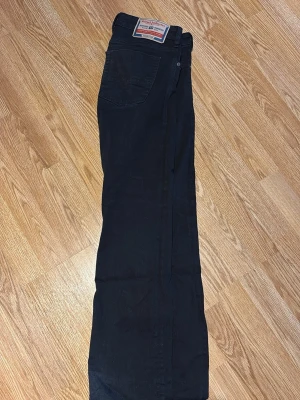 Svarta raka jeans från Diesel - Säljer ett par svarta jeans från Diesel med klassisk rak passform. Jeansen har fem fickor, bälteshällor och en tydlig Diesel Industry-lapp bak i midjan. Tillverkade i slitstarkt denimtyg som passar perfekt till en avslappnad streetstil. Bootcut