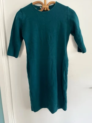 Mörkgrön klänning i ull - Snygg figursmickrande mörkgrön klänning i mjuk merinoull med enkel, rak passform och trekvartsärm. Perfekt till dig som gillar stilrena plagg med skön känsla. Klänningen har rund halsringning och slutar strax ovanför knät.