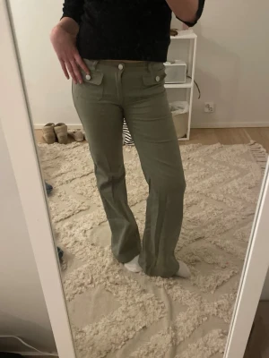 Gröna bootcut jeans med fickor - Snygga gröna jeans med bootcut-modell och höga fickor fram. Jeansen har vida ben och stängs med två knappar och dragkedja. Perfekta för dig som vill ha en cool och avslappnad stil. Materialet ser ut att vara denim med lite stretch.
