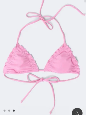 Rosa bikini med knyt och volang - Endast använd 1gång. Supersöt rosa bikini med trekantsmodell på toppen och knyt både i nacken och ryggen. Underdelen har knyt i sidorna och diskreta volangdetaljer längs kanterna. Perfekt för lata dagar på stranden eller poolen.