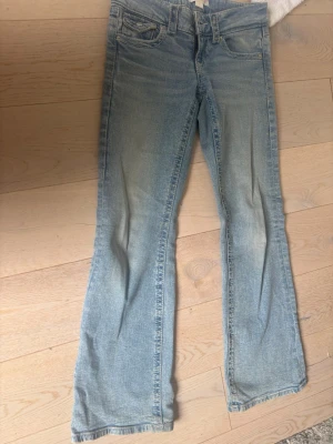 Ljusblå bootcut jeans med ficklock - Säljer ett par ljusblå bootcut jeans med klassisk femficksmodell och snygga ficklock med knapp bak. Jeansen har en lätt tvättad look och är tillverkade i denim med skön stretch. Dom är i väldigt bra skick.