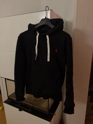 Ralph lauren hoodie  - Säljer min svarta hoodie från Ralph lauren med vit snöring och röd broderad logga. Använts väldigt få gånger och skicket är som nytt. Tröjan kan även bäras som XS. Extremt prisvärt för skicket!
