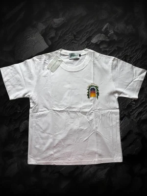 Casablanca tröja  - Vit t-shirt med färgglatt tryck på bröstet och stort motiv på ryggen med texten 'Avenida Casablanca' och ett palats i solnedgång. Klassisk passform och rund halsringning. Perfekt för dig som vill sticka ut med en unik design.