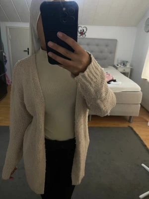 Beige stickad öppen kofta - Mysig beige stickad kofta med öppen front och långa ärmar. Koftan har en avslappnad passform och ribbstickade muddar vid ärmslut. Perfekt att slänga över en topp för en chill look.