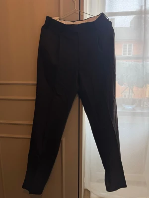 Svarta kostymbyxor från Suitsupply - Stilrena svarta kostymbyxor från Suitsupply i modellen Wide Leg Straight Trousers. Tillverkade i 100% ull för en lyxig känsla och snygg passform. Klassisk design med pressveck och raka ben, perfekta till skjorta eller kavaj.